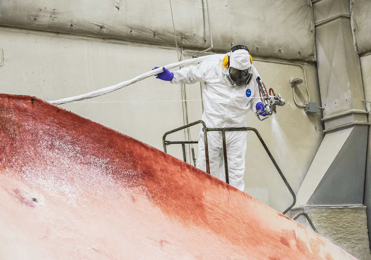 Employee spraying fiberglass resin chop on mold